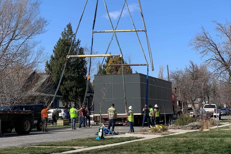 Crowd of construction workers guiding a small home off of a flatbed trailer