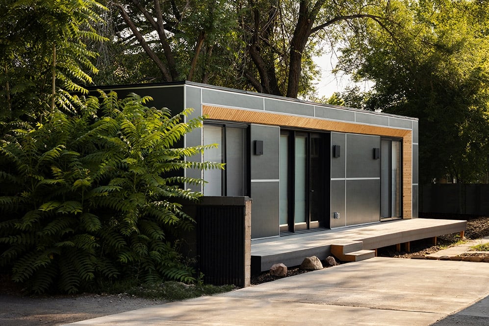 A modern ADU from Modal in a sunlit backyard with green trees.