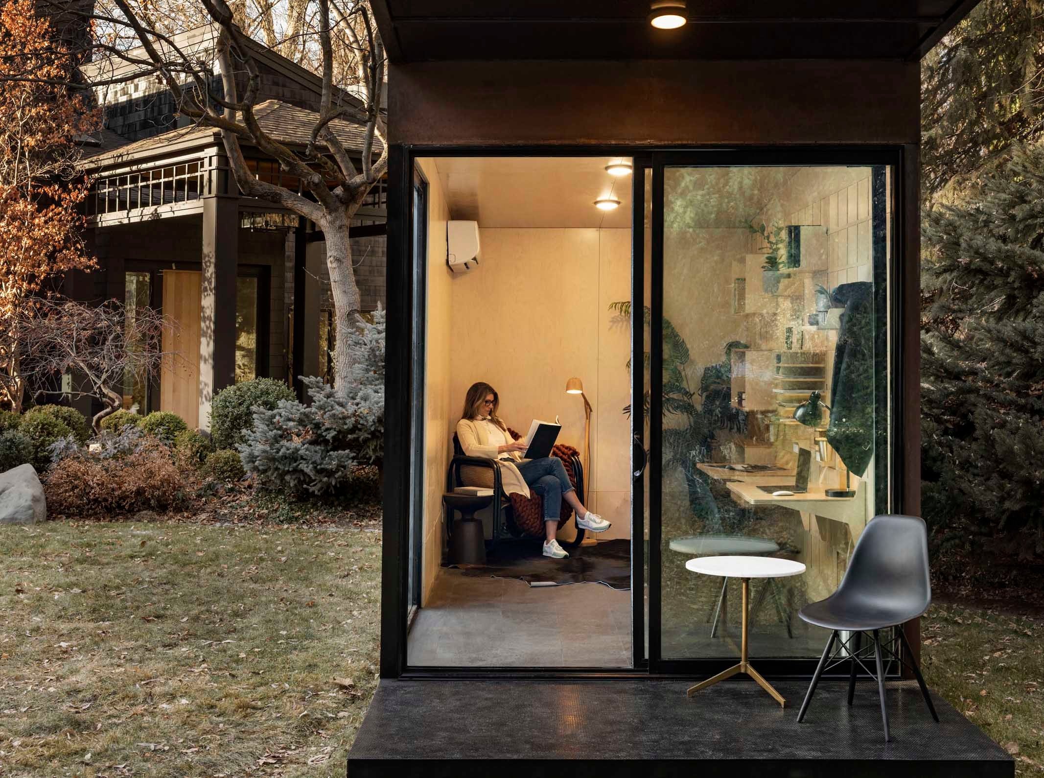 Modal Pod unit sitting on the grass in a backyard with a lady reading inside