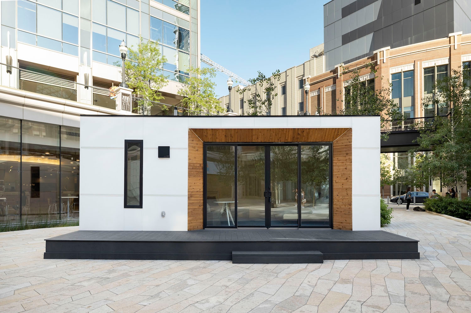 A small prefab home sitting in the courtyard of a city mall to function as a showroom