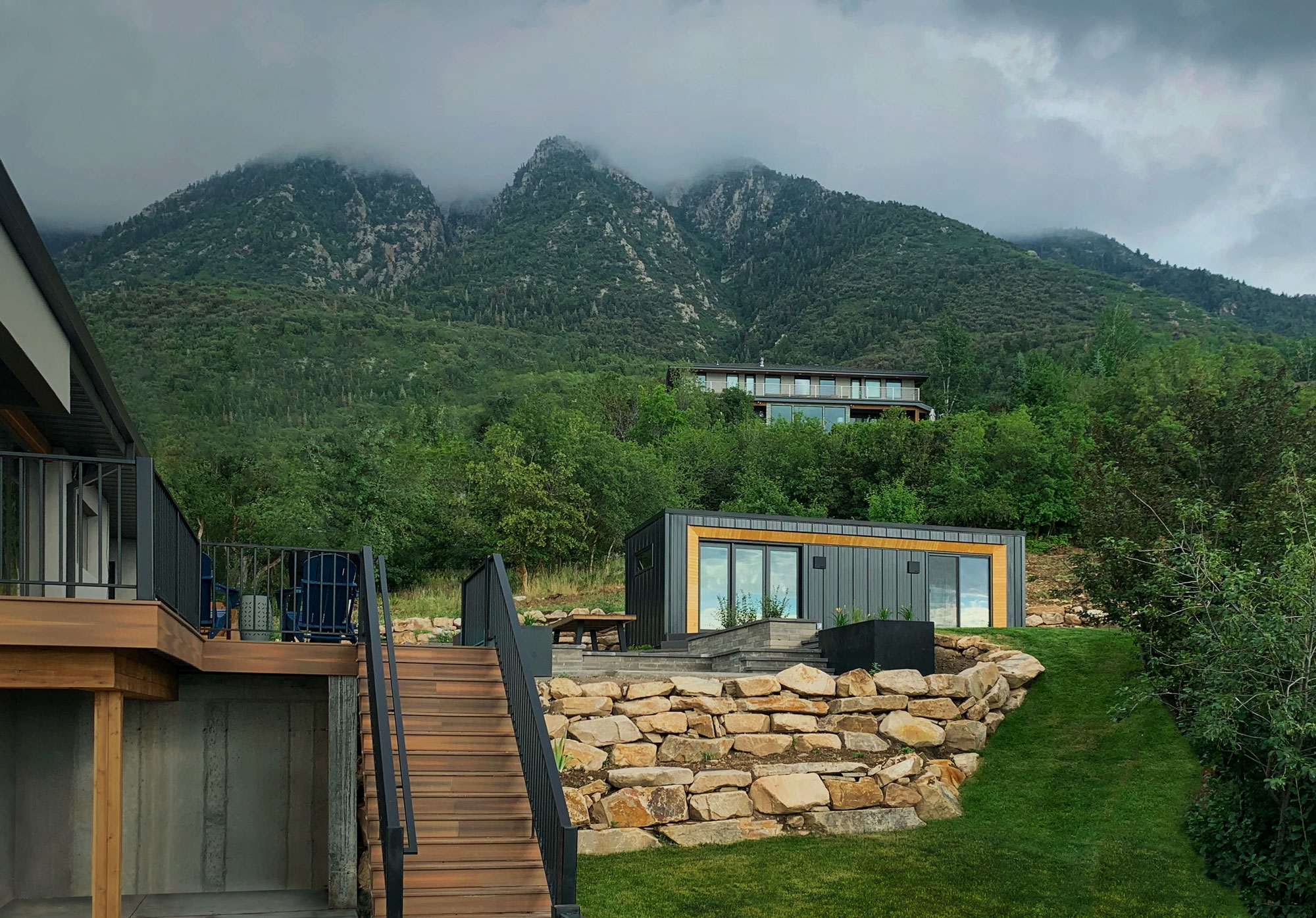 A Modal 01 accessory dwelling unit with black paneling and cedar trim sitting comfortably behind a large rock wall